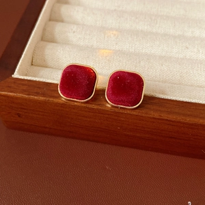 Macro detail of red flocked square stud earrings with gold metal trim on jewelry tray