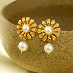Macro shot of gold floral earrings with hanging pearls on a rustic ceramic edge