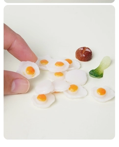 Macro detail of miniature fried egg and mushroom PVC models held by a hand