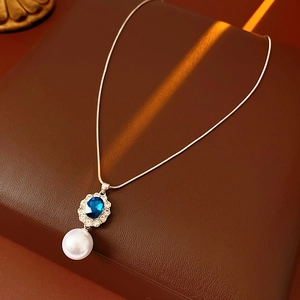 Dettaglio macro di una collana vintage con pietra blu e perla bianca su pelle marrone