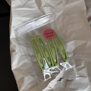 Detail of four avocado green matte bobby pins in a clear package with a minimalist design