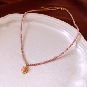 Detail of pink beaded necklace with gold oval pendant on a decorative white porcelain plate