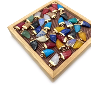 Chili-shaped natural stone pendants with gold-plated caps in various colors on a wood tray