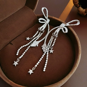 Détail des boucles d'oreilles argentées à pompons avec étoiles et nœuds dans un écrin