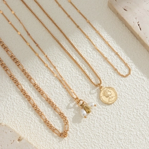 Detailed macro of gold-layered necklace set with coins and faux pearls on stone background