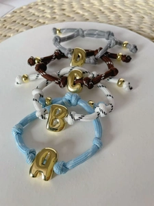 Detail von DIY-Seilarmbändern mit glänzenden 18K vergoldeten Buchstabenanhängern.