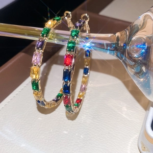 Detailed close-up of gold hoop earrings with multi-colored rectangular zircons on glass stem
