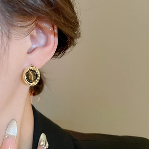 Detail of vintage gold-plated tiger eye stud earrings on model with a retro textured design