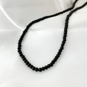 Macro detail of elegant black onyx beaded necklace on white silk fabric background