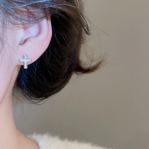 Close-up of sparkling silver cross earrings with zircon stones worn by a female model