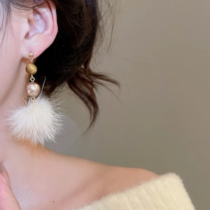 Nahaufnahme von eleganten Tigerauge-Perlen und weißen Pompon-Ohrringen an einem Modell