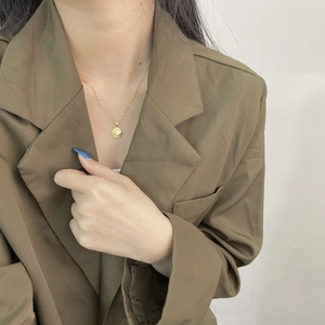 Close-up of a gold 925 sterling silver evil eye pendant worn on a brown blazer outfit
