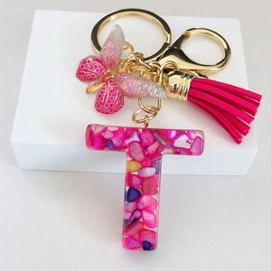 Detail of pink resin letter T keychain with golden butterfly and soft tassel