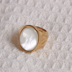 Dettaglio macro di un anello a sigillo dorato con madreperla ovale su tessuto a maglia