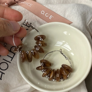 Detail of large silver hoop earrings with brown marble-textured beads on fabric