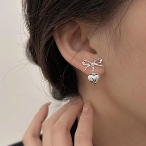 Polished 925 sterling silver bow and heart stud earrings worn by a female model