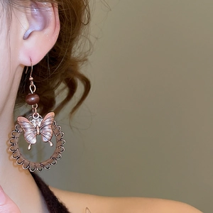 Macro detail of retro bronze butterfly hoop earrings with wooden beads on model ear