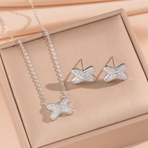 Silver bow-shaped necklace and earrings set with micro-pave crystals on soft beige fabric
