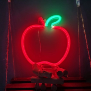 Apple-shaped LED neon light with red glow and green leaf on rustic wooden stand