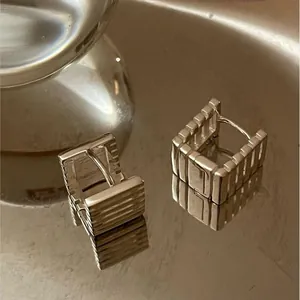 Macro shot of silver geometric earrings with vertical stripes on a metallic tray