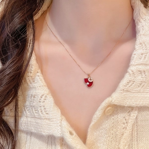 Close-up of a gold necklace with a red heart pendant and cubic zirconia on a model