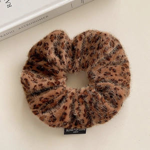 Detail of leopard print plush scrunchie with a black woven brand label on white surface