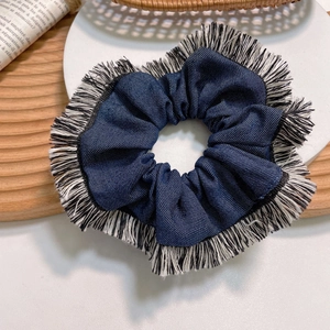 Denim blue large scrunchie with white fringe edges on a rustic display stand
