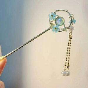 Detailed shot of golden metal hair pin with blue flowers, pearls, and tassel chain