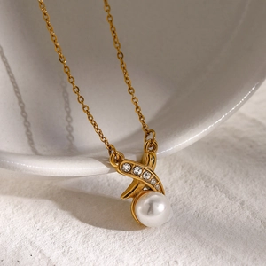 Detailed shot of an 18k gold plated X-shaped pendant with diamonds and a white pearl