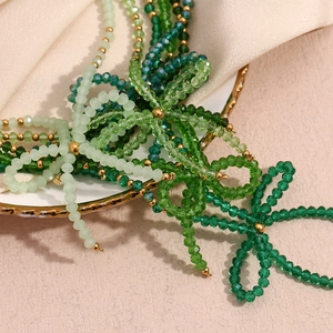 Detailed view of green crystal beads and gold metal spacers on smooth silk fabric