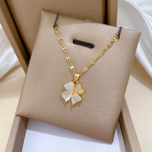 Detailed macro view of a gold clover necklace featuring white shells and a crystal heart