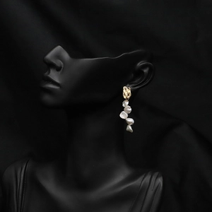 Close-up of golden tassel earrings with white baroque pearls on a black model silhouette