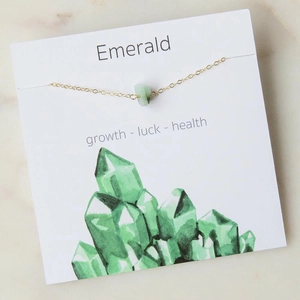 Gold chain necklace with irregular green emerald stone pendant on white marble background