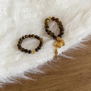 Tiger eye stone bead ring set with golden horse and coin charms on white plush background