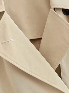 Detail of premium beige twill trench coat showing precise stitching and dark button