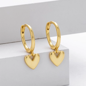 Detailed close-up of polished golden heart drop earrings on a minimalist white stand