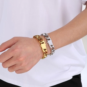 Detail of 13mm gold and silver stainless steel Cuban link bracelets on male wrist