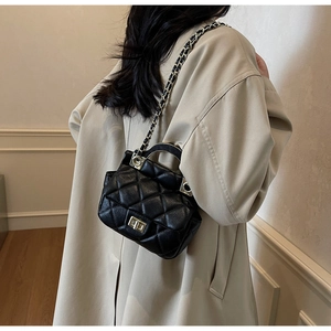 Detail of black quilted leather handbag featuring a gold turn-lock and chain strap