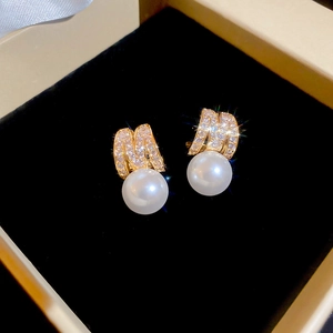 Macro shot of gold letter M earrings with pavé zircons and a white pearl drop