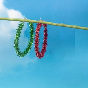 Festive red and green tinsel hoop earrings hanging against a clear blue sky