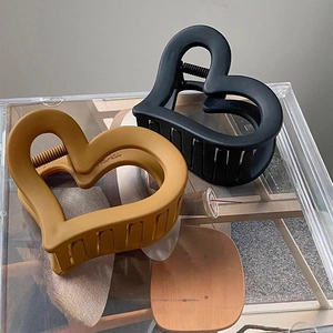 Matte black and yellow heart-shaped hair claw clips for women on a wooden coaster