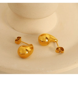 Close-up of 18K gold plated teardrop stud earrings resting on a ceramic vessel rim