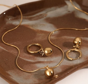 Macro view of gold-plated stainless steel 3D red apple necklace and matching earrings