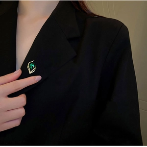 Elegant emerald leaf brooch with gold metal and diamonds pinned on a black suit lapel