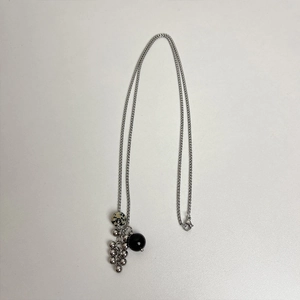 Détail de collier argenté avec perles noires, pierre tachetée et pompon métallique chic