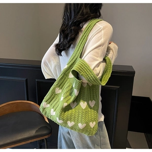Vista lateral de un bolso tote de punto verde con patrones de corazones blancos de modelo