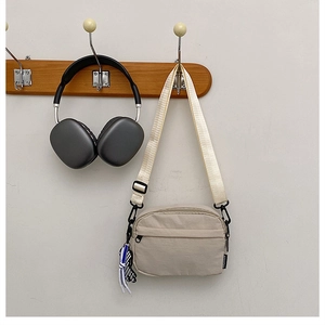 Détail du sac bandoulière beige en nylon avec poche zippée et breloque en damier