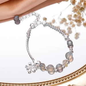 Detailed view of silver flower charm bracelet with grey translucent beads on a mirror