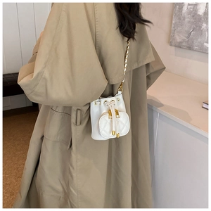 Detail of white quilted mini bucket bag with gold chain strap on khaki trench coat