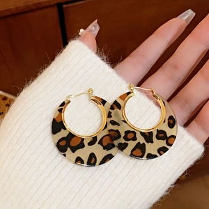 Close-up of leopard print hoop earrings with gold clasp on a beige knit background